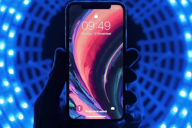 A smartphone held in a person's hand displays a vibrant, abstract wallpaper. The screen shows the time as 09:49 and the date as Monday, 13 November. The background is a blue circular pattern illuminated by lights.