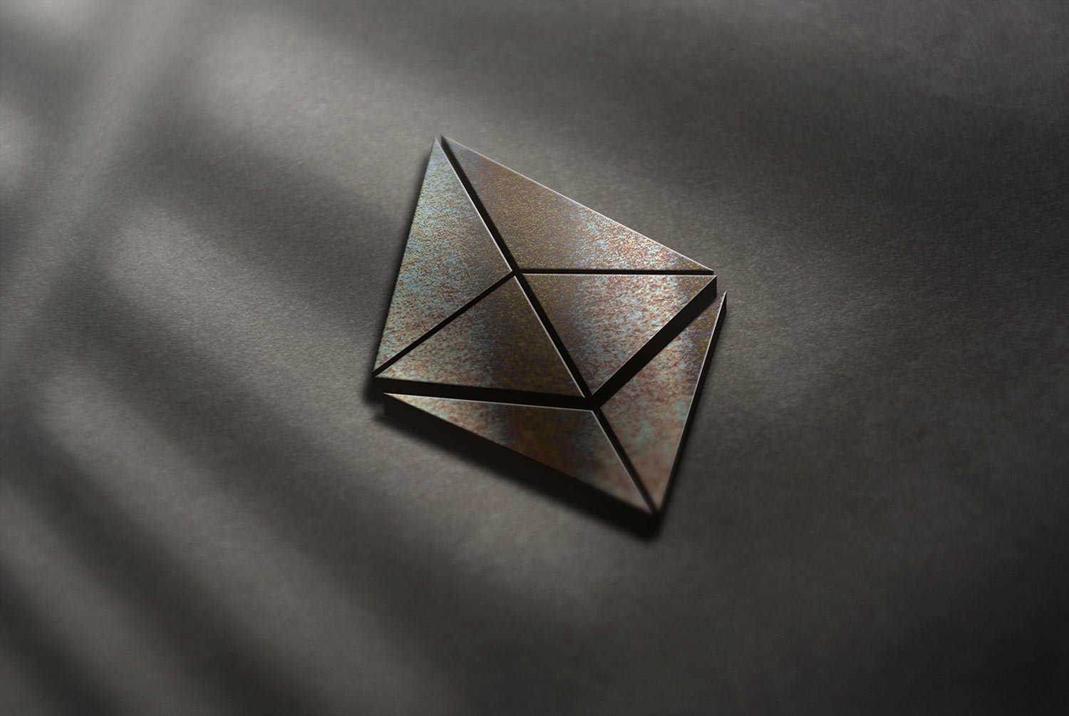 A shiny, metallic Ethereum logo is centered on a dark surface. Soft light filters across, creating gentle shadows. The logo's geometric shape is emphasized by its reflective texture.