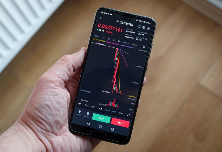 A person holds a smartphone displaying a cryptocurrency trading app. The screen shows a price chart for UST/BUSD with a significant downward trend. Options to buy and sell are visible at the bottom of the screen.