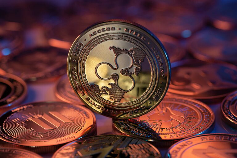 Close-up of cryptocurrency coins, with a focus on a Ripple (XRP) coin standing upright. The coin has a map design and the XRP logo, surrounded by other coins in warm lighting.