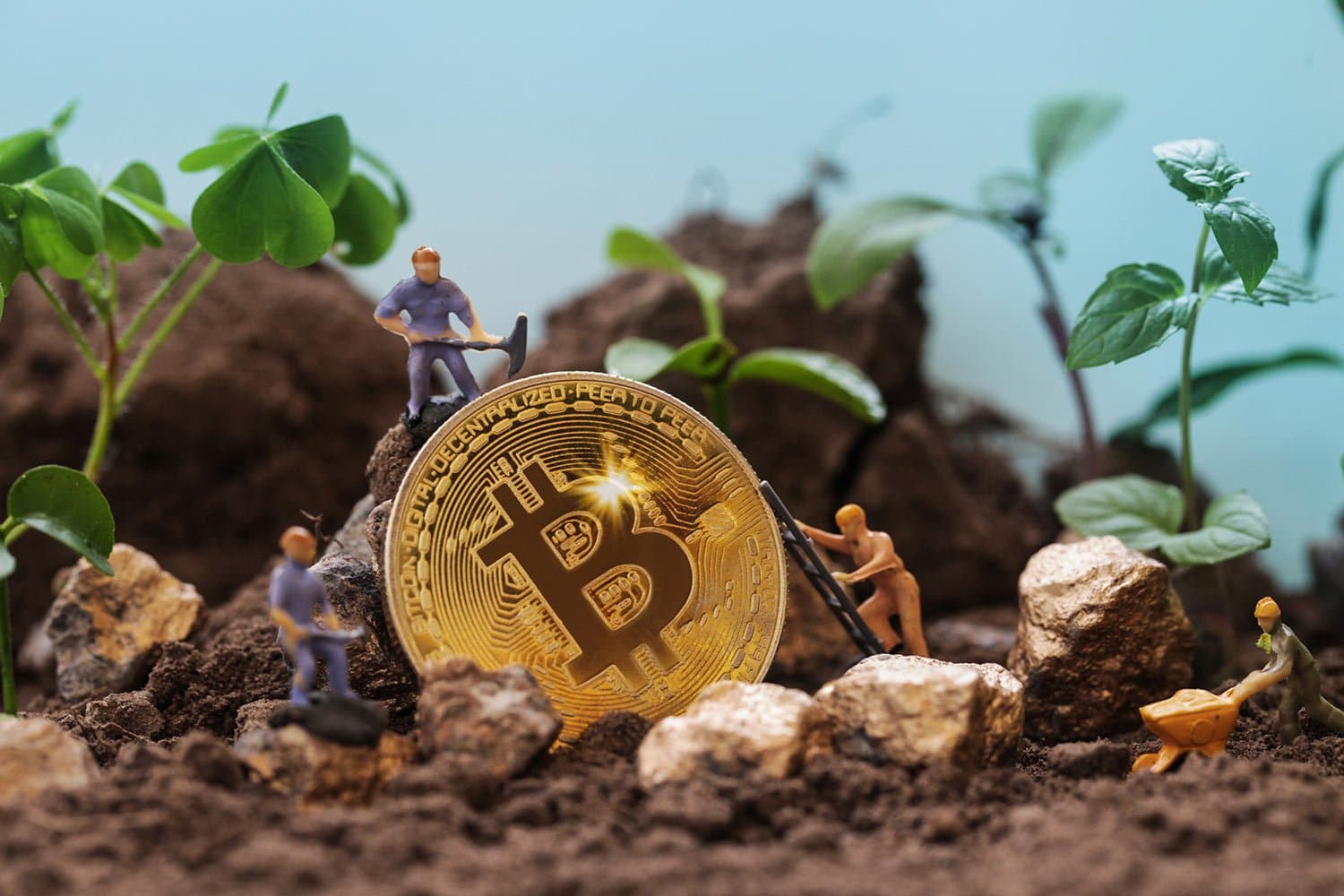 Toy figurines are digging around a large, golden Bitcoin coin surrounded by soil and small plants. This scene symbolizes the concept of "mining" Bitcoin, blending digital currency with natural growth imagery.